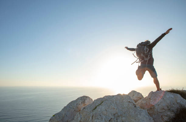 Hiker jumps across mountain ridge at sunrise Mediterranean Sea in the distance leap of faith stock pictures, royalty-free photos & images