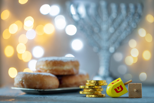 Hanukkah concept with menorah, sufganiyah, wooden dreidel, chocolate coins and bright light in the background