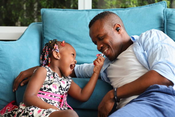 african american ojciec bawi się ze swoją małą córką, którzy karmią go czekoladą, spędzając szczęśliwy czas razem w domu - family american culture african culture black zdjęcia i obrazy z banku zdjęć