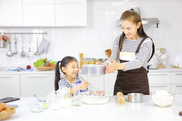 mãe asiática feliz ensinando sua filha jovem a assar pão na cozinha branca moderna enquanto peneirava farinha de trigo - bread food baked 7 grain bread - fotografias e filmes do acervo