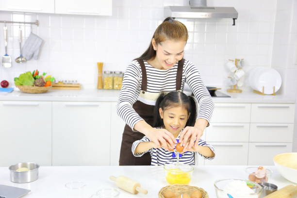 feliz madre asiática enseñando a su hija pequeña rompiendo huevo para mezclar con harina a pan hornear en la cocina blanca - bun bread 7 grain bread dough fotografías e imágenes de stock