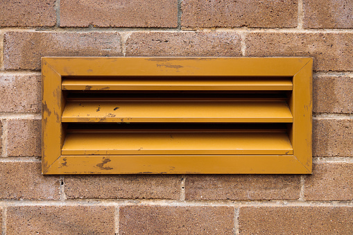 Yellow metal mail slot in a brick wall.