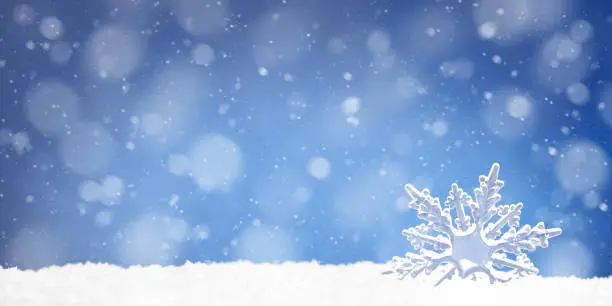 Photo of Toy snowflake in a snowdrift on blue background, copy space