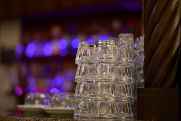 Small glass transparent cups with neat stack vertical rows on the bar. Amid the lights side of the showcase.