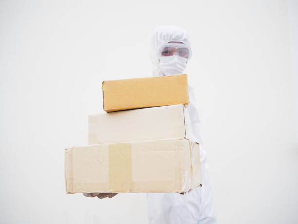 istock Young man in PPE suite uniform while holding cardboard boxes in medical rubber gloves and mask. coronavirus or COVID-19 concept isolated white background 1283313690