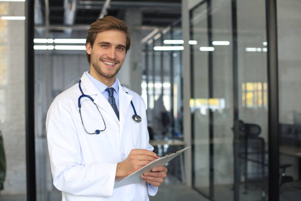 istock Handsome friendly young doctor on hospital corridor looking at camera, smiling. 1283313726