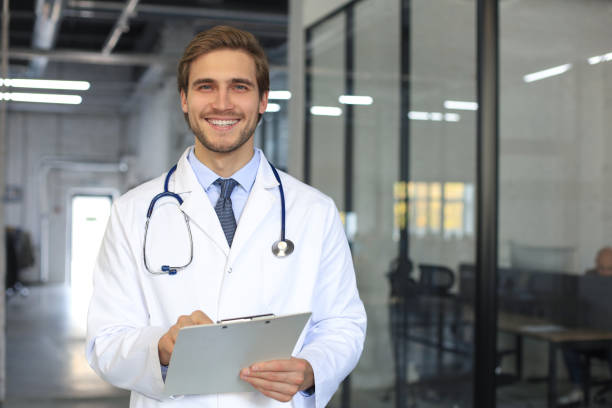 istock Handsome friendly young doctor on hospital corridor looking at camera, smiling. 1283313732