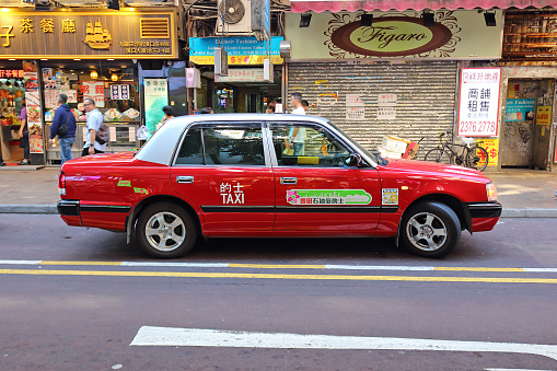 Hong Kong, China - October 6, 2018: Iconic transportation vehicle in Hong Kong is red urban taxi cab Toyota Crown Comfort. Selective focus and blurred motion a pedestrian on background