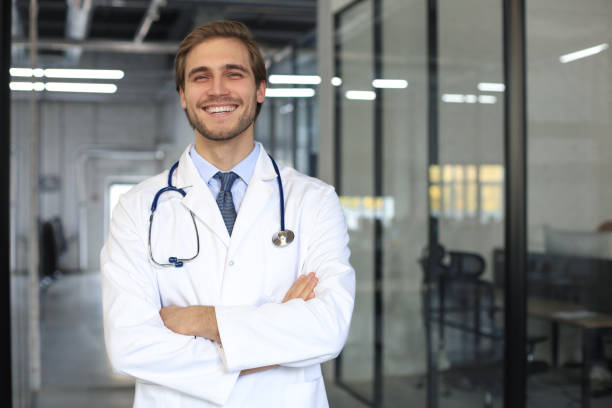 istock Handsome friendly young doctor on hospital corridor looking at camera, smiling. 1283313738