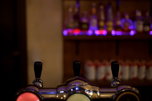 The handles of the bottling system in the bar, alcohol beer, against the background of the showcase with bottles in the illumination of lilac color.