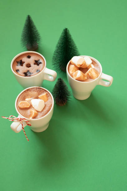 istock White cups with hot cocoa, marshmallows, spice cinnamon decor and Christmas fir tree decor on green background. Winter holidays drinks, vertical 1283319657