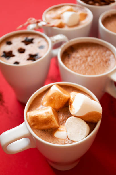 istock Close-up hot cocoa with marshmallows in white cups on red background, vertical 1283319755