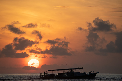 A group of people are fishing off the back of a boat in the Maldives on a traditional Maldivian Dhoni at sunset