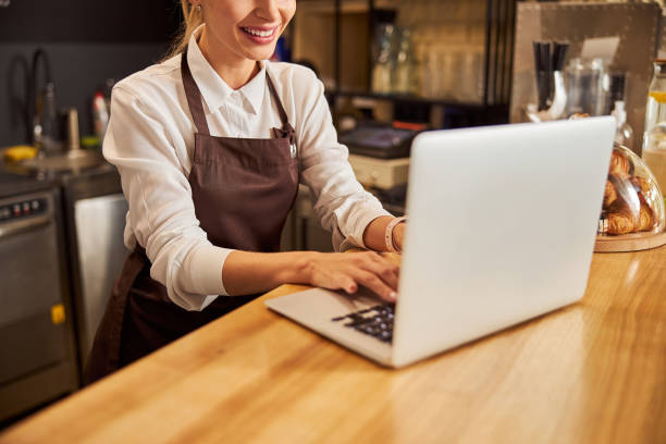 istock Saleswoman in uniform typing report on the computer in coffee bar 1283322193