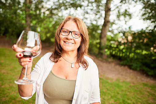 Portrait of a smiling mature woman drinking a glass of red wine in her yard in the summer