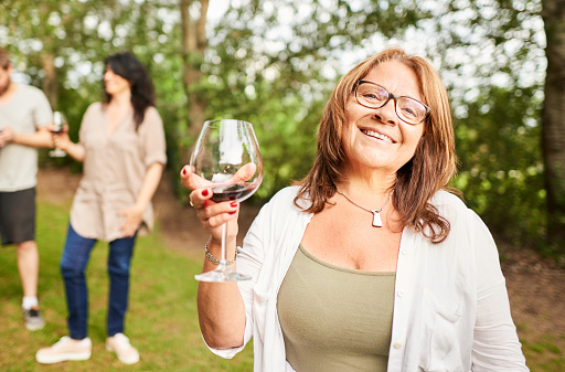 Portrait of a smiling mature woman holding a glass of red wine during a garden party in the summer