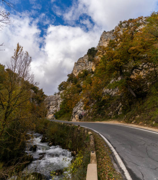 istock fall color forest and rocky cliffs with a winding mountain road next to a small river 1283323296