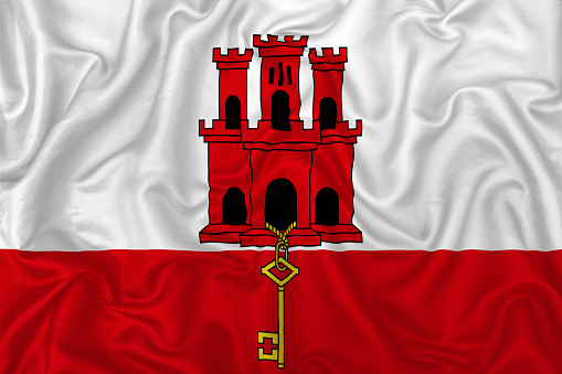 Gibraltar flag on wavy silk textile fabric background.