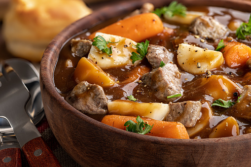 Closeup of a wooden bowl of beef stew with carrots and potatoes