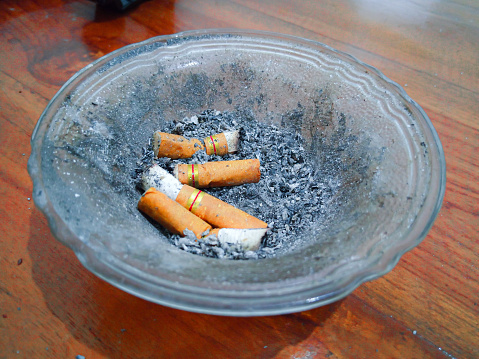 Ashtray with cigarette butts close-up. Dark blurred background, no focus, smoking harm concept
