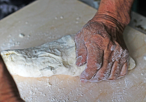 Old male Hands close-up man making dough for homemade noodles, dumplings on wooden board with wheat flour