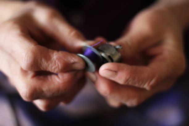 istock Old woman hands fingers threading a bobbin with lilac thread into the shuttle of an sewing machine 1283328708