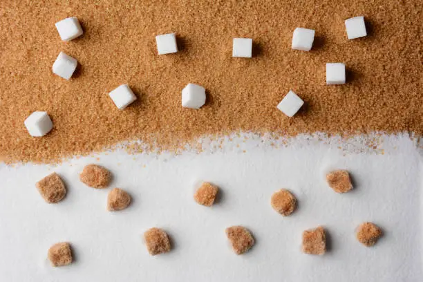 White and brown sugar contrast. White sugar cubes on raw brown turbinado granules and raw brown sugar lumps on white granulated sugar.