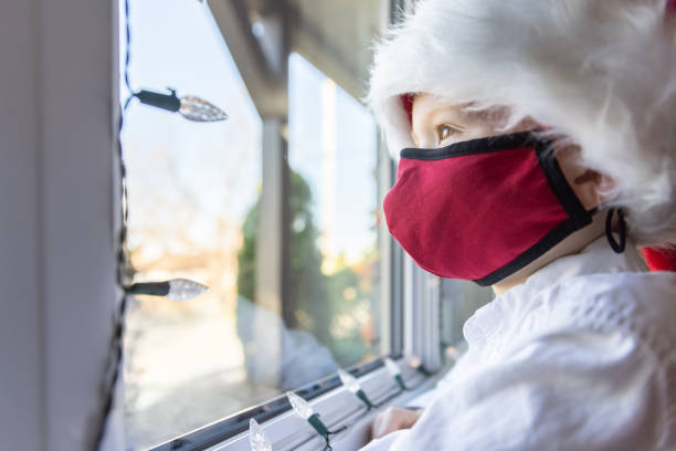 istock Young Boy wearing protective face mask and santa hat looking through the window during the Covid-19 Pandemic 1283333571
