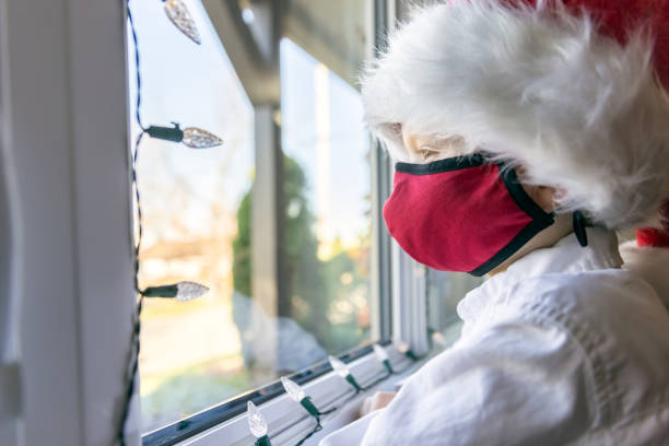 istock Young Boy wearing protective face mask and santa hat looking through the window during the Covid-19 Pandemic 1283333684