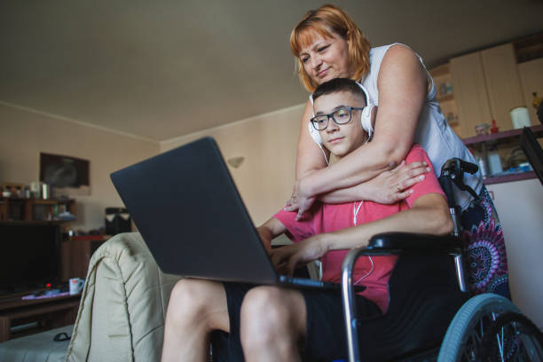 un adolescent en fauteuil roulant travaille sur un ordinateur portable et communique avec des amis - disabled teenager adolescence physical impairment photos et images de collection
