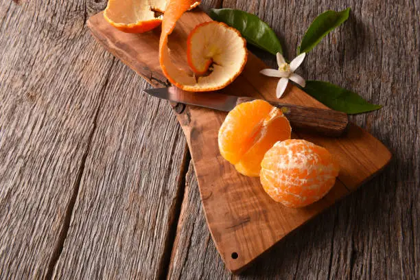 Closeup of a fresh peeled Minneola Tangelo on a cutting board with knife and orange blossoms.