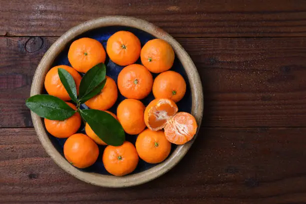 Top view of a plate of fresh ripe Mandarin Oranges in a rustic wood table with one peeled piece of fruit.