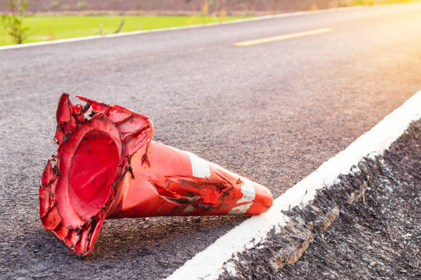 The orange rubber cone was wrecked, falling on a paved road. Close-up of the demolished orange rubber cone laying on the ground of an asphalt road in the early morning Thai countryside. traffic cone photos stock pictures, royalty-free photos & images