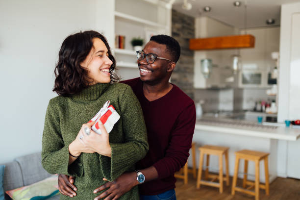 Interracial young couple celebrating Valentine's day Happy young interracial couple having fun at home, African American boyfriend surprising his Caucasian girlfriend with a Valentine''s day present, making her smile valentines day holiday stock pictures, royalty-free photos & images