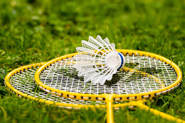 shuttlecock bianco su racchette badminton giallo nell'erba verde - racchetta da volano foto e immagini stock