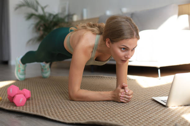 istock Fitness woman doing plank and watching online tutorials on laptop, training in living room. Stay at home activities. 1283349007