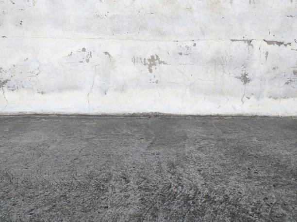 istock Front view of White concrete exterior wall with gray concrete floor. Pattern. Uncorked cement wall and dark gray asphalt. Urban construction detail. Old White-painted Concrete Wall Background. 1283351252