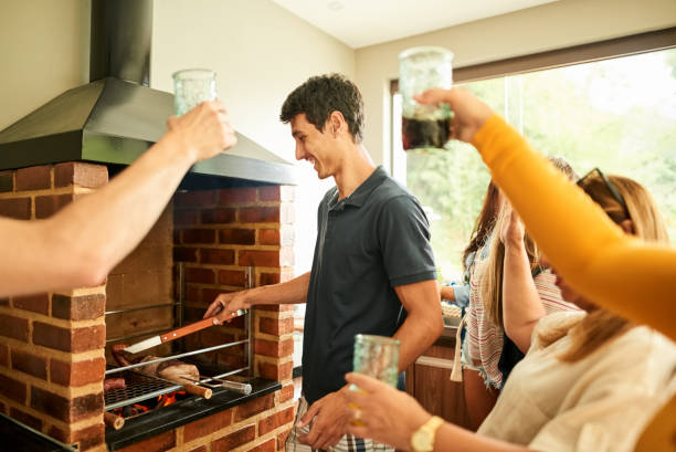 Best bbq chef in the house Shot of man barbecuing meat on the grill in kitchen with friends cheering with soft drinks brazilian bbq stock pictures, royalty-free photos & images