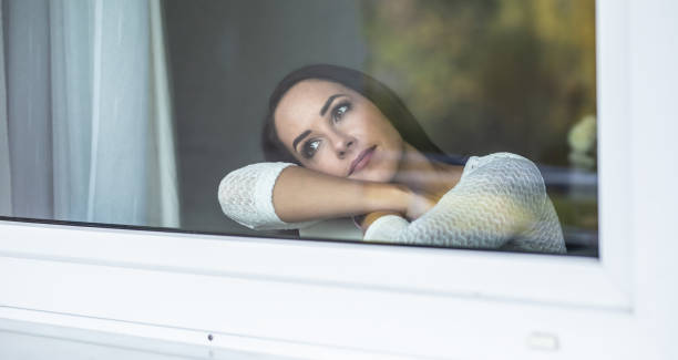 istock Daydreaming woman rests her head on her elbow on a window sill looking out. 1283358518