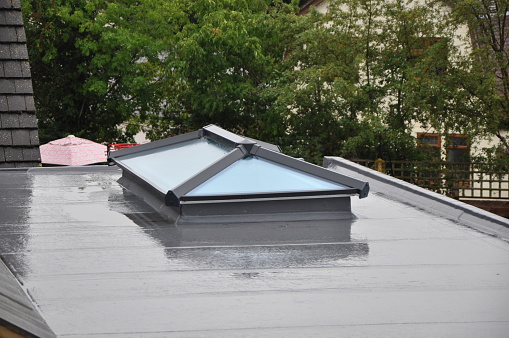 Modern glass roof lantern or light on contemporary grey flat roof in the rain