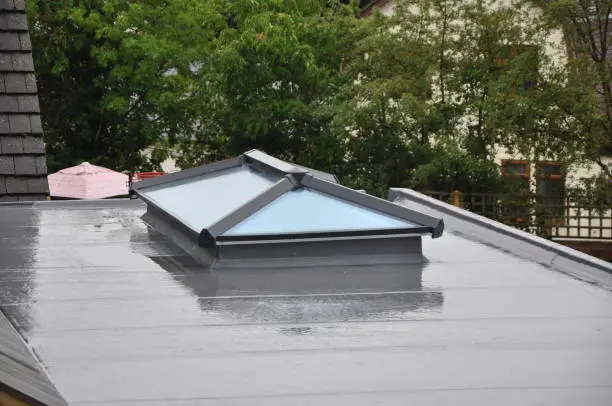 Contemporary, modern, luxury, double glazed glass roof lantern or light on a grey flat roof building or extension. Rainy autumn day, with reflections in rainwater on the roof surface