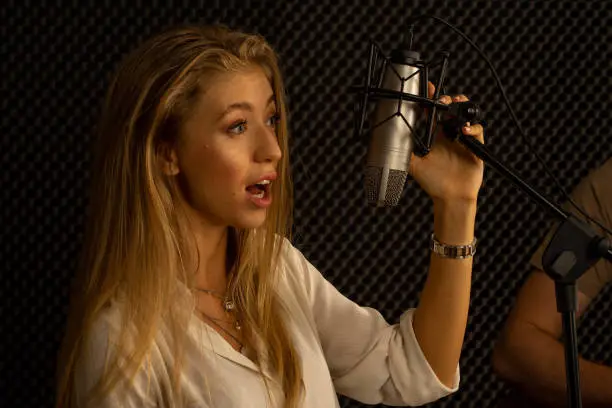 young attractive Caucasian woman musician singer in recoding studio with microphone. Performance arts concept.