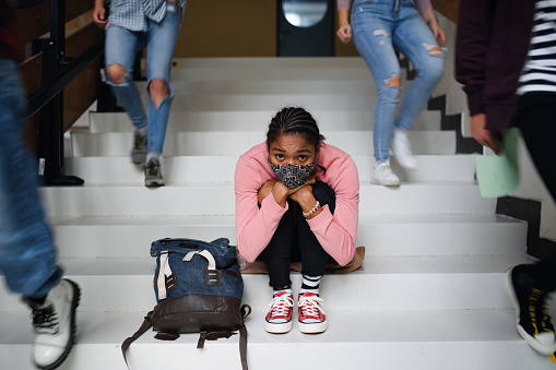 Depressed young student with face mask sitting and studying on floor back at college or university, coronavirus concept.