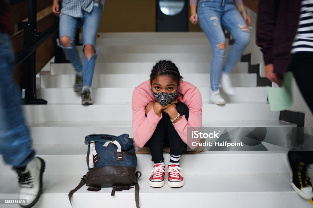 Depressed young student with face mask sitting on floor back at college or university, coronavirus concept. Depressed young student with face mask sitting and studying on floor back at college or university, coronavirus concept. Mental Health Stock Photo