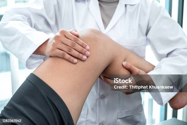 Female Physiotherapist Working Examining Treating Injured Leg Of Patient Doing Exercises The Rehabilitation Therapy Pain His In Clinic Stock Photo - Download Image Now