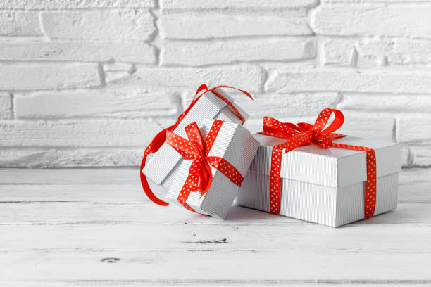 istock Set of gift boxes with red ribbon on a white wooden table, brick backdrop. Selective focus, copy space 1283367141