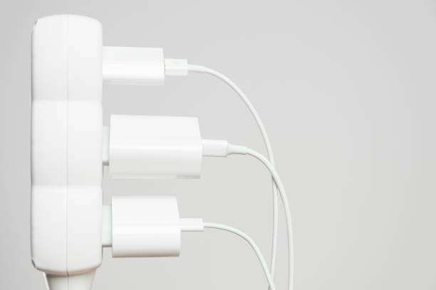 Indoor white office extension cord with three white connected to it various size power plugs with copy space. Smart phones chargers in power strip for electrical sockets.