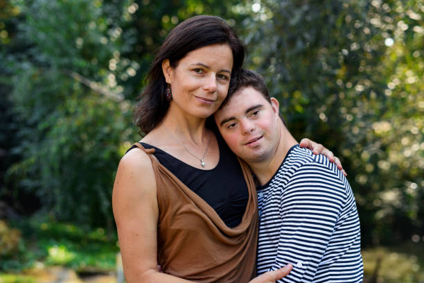 Portrait of down syndrome adult man with mother standing outdoors in garden. Portrait of down syndrome adult man with mother standing outdoors in garden, looking at camera. down syndrome photos stock pictures, royalty-free photos & images