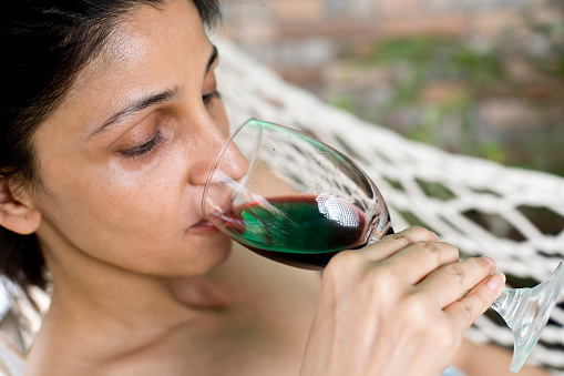 Happy woman relaxing in hammock with a glass of red wine