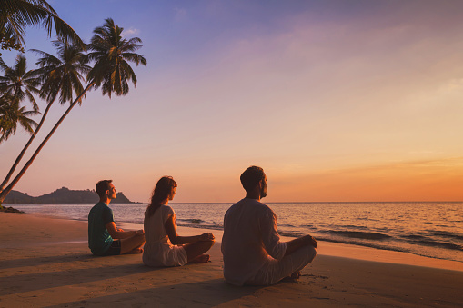 yoga retreat on the beach at sunset, silhouettes of group of people meditating